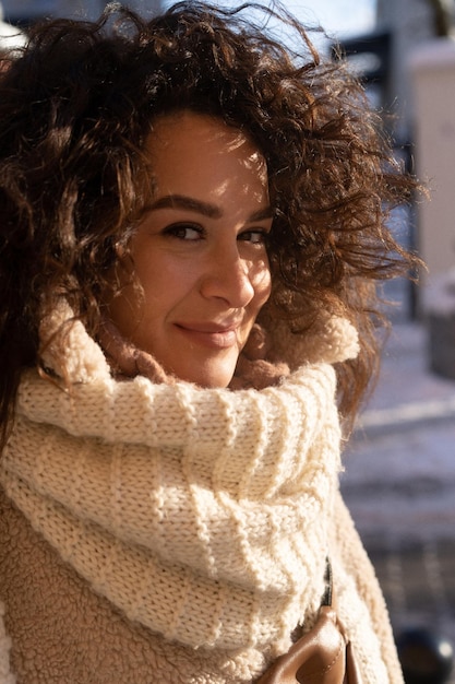 Young woman with dark curly hair, warmly dressed fur coat, scarf, winter frost, sunny day on the street in the city.