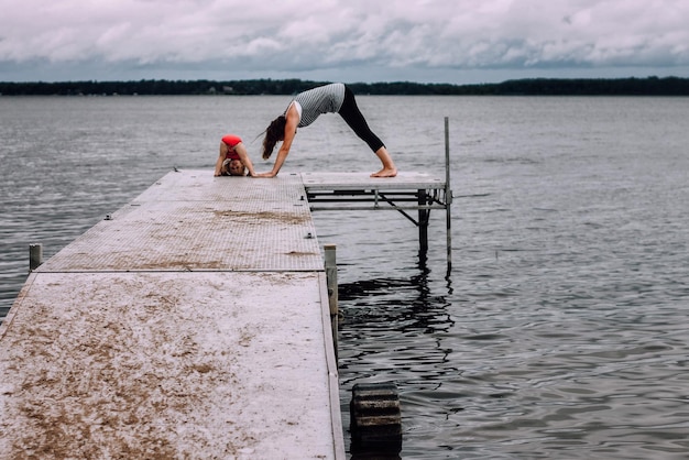 Foto giovane donna con la figlia che fa yoga sul molo sopra il lago