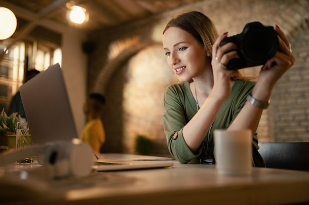 Young woman with digital camera using computer while working late in her studio