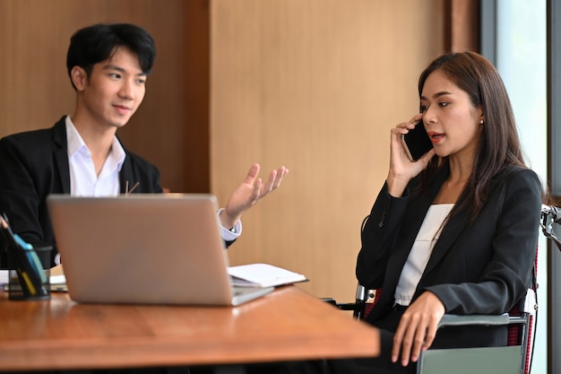 オフィスで同僚と一緒に働いている車椅子の障害を持つ若い女性。