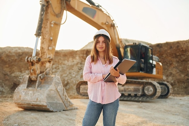 Photo young woman with documents in hard hat is standing on the borrow pit