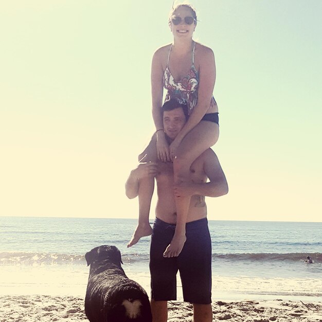 Young woman with dog standing on beach against sky