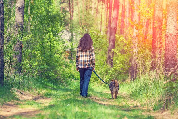 Young woman with dog walking in the forest at sunset