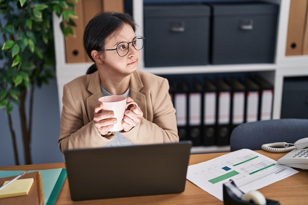 Молодая женщина с синдромом Дауна, деловая женщина, пьющая кофе в офисе с ноутбуком