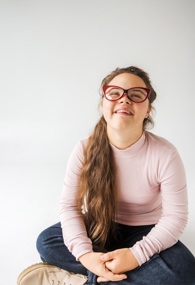 Photo a young woman with down syndrome sits crosslegged against a white background wearing a pink longslee