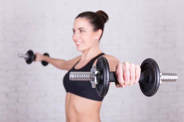 Young woman with dumbbells over white brick wall