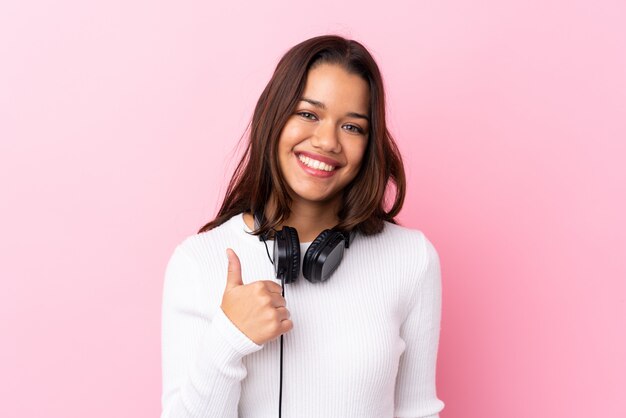 Young woman with earphones over pink wall with thumbs up because something good has happened