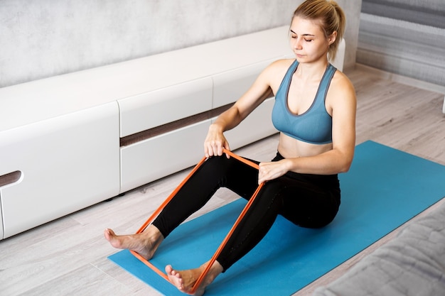 Young woman with elastic band. She trains her legs at home