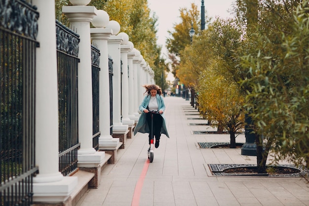 Young woman with electric scooter in blue coat at the city