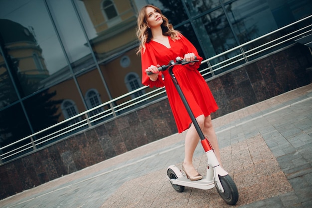 Young woman with electric scooter in red dress at the city