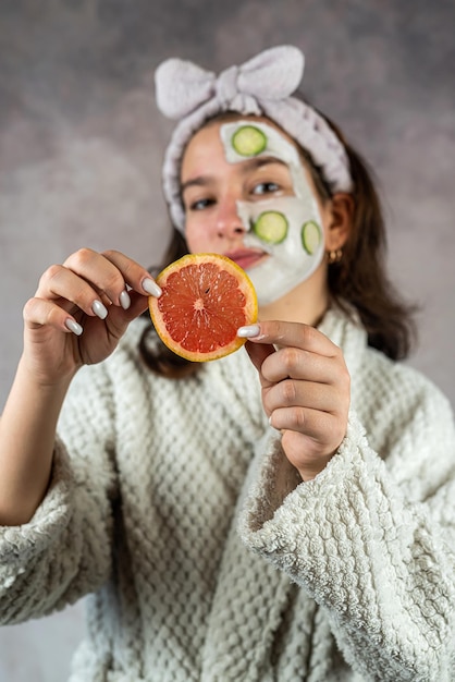 Young woman with a face clay mask and grapefruit cucumbers