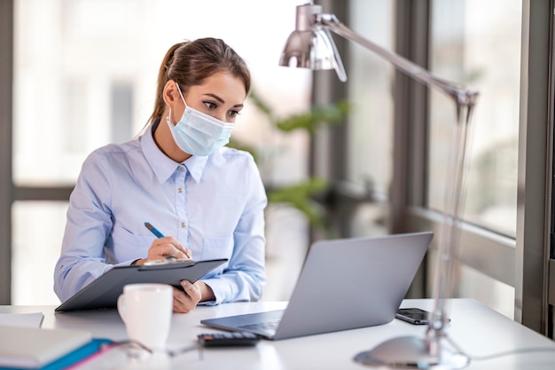 Young woman with face mask back at work in office