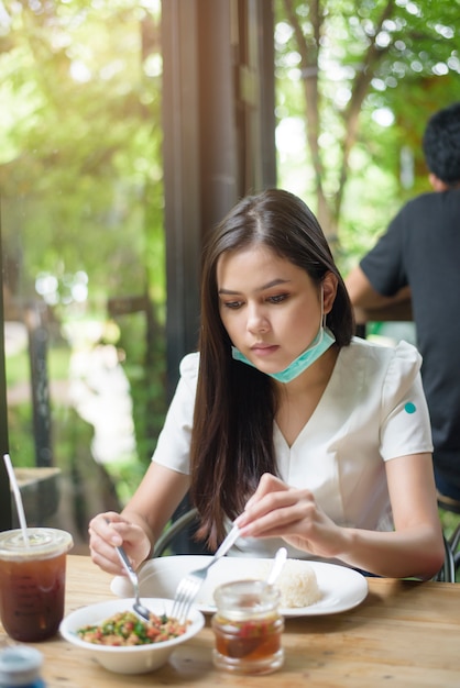 フェイスマスクを持つ若い女性はレストラン、新しい通常のコンセプトで食べ物を持っています。