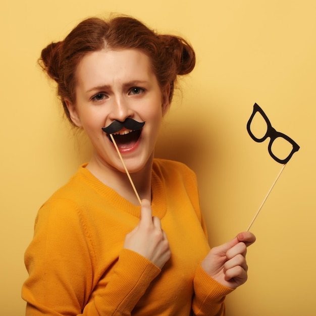 Young woman with fake mustaches and glasses over yellow backgro