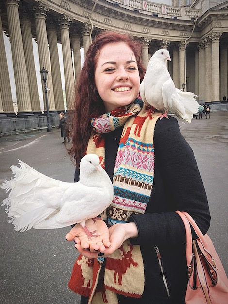 Foto giovane donna con piccioni a coda che si appoggiano sulle mani mentre si trova contro la cattedrale di kazan
