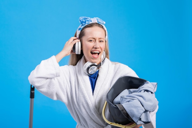 Young woman with floor mop listening to music on color background