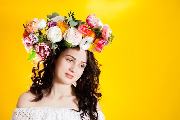 The young woman with a flowered wreath on her head, isolated on a yellow background