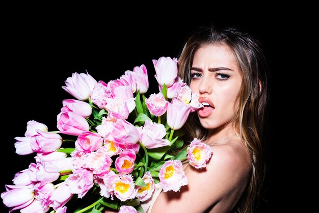 Young woman with flowers. Beautiful girl holding bouquet of tulips over black background sticking tongue with sexy expression.