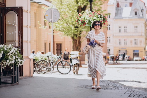 Giovane donna con fiori che cammina in città