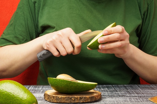 Young woman with fresh avocado at the table. the girl is cleaning a green avocado. the process of preparing healthy food