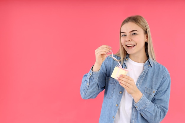 Young woman with gift box on pink background