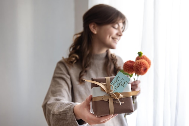 Young woman with a gift for mothers day and a bouquet of flowers in her hands