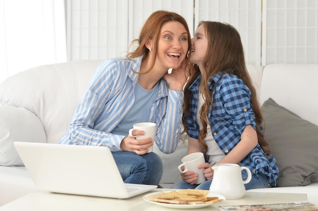 Young woman with girl sharing secret on sofa at home