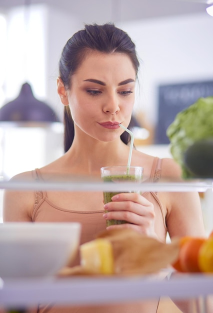 Young woman with glass of tasty healthy smoothie at table in kitchen