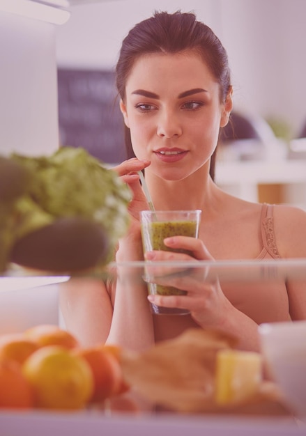 Foto giovane donna con un bicchiere di gustoso frullato sano a tavola in cucina