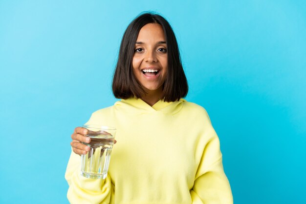 Young woman with a glass of water isolated on blue wall with surprise facial expression