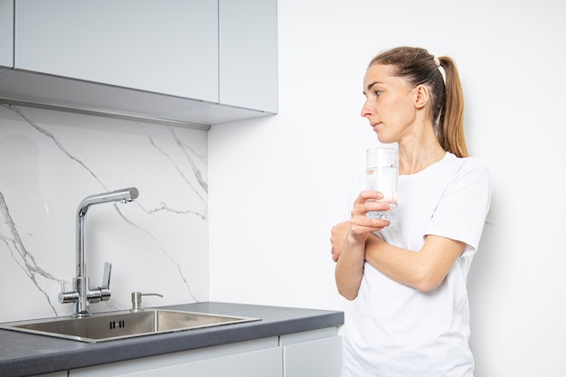 Photo young woman with a glass of water standing in the kitchen