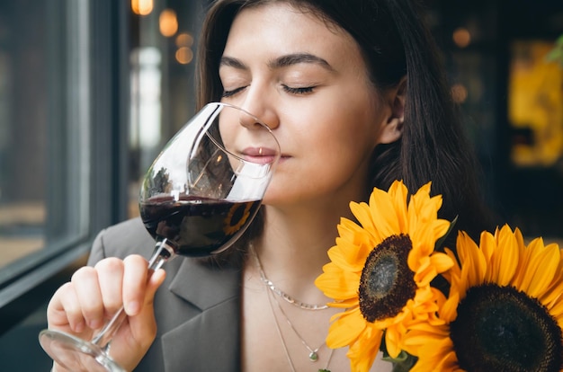 Una giovane donna con un bicchiere di vino e un bouquet di girasoli in un ristorante