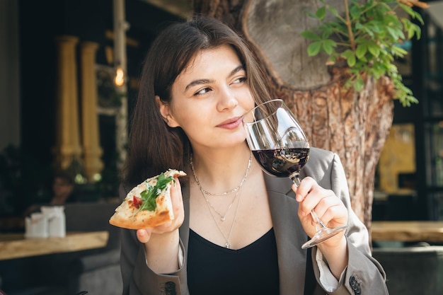 A young woman with a glass of wine and a slice of pizza in a restaurant