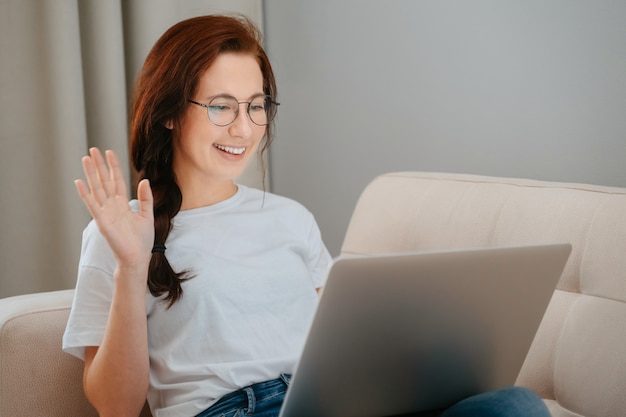 Photo young woman with glasses communicates online on a laptop while sitting at home bright sofathe concep...