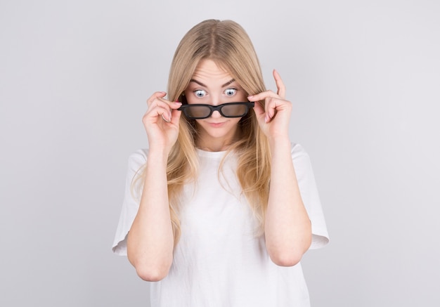 Young woman with glasses is very surprised looking down and lowering her glasses. Surprise and shopping concept on white background.