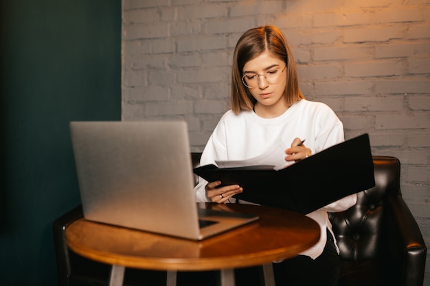 Фото Молодая женщина в очках писать и использовать ноутбук в кафе-баре