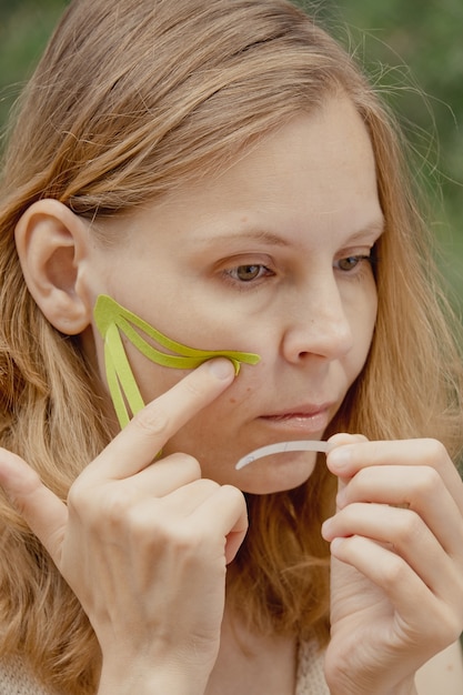 Giovane donna con nastri verdi sul viso taping estetico viso