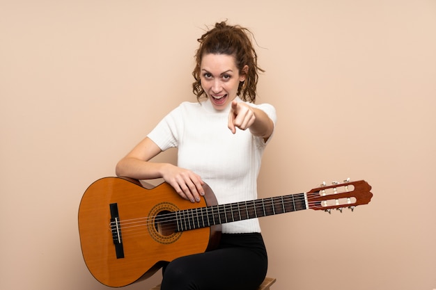 孤立した驚きとポインティングフロント上のギターを持つ若い女性