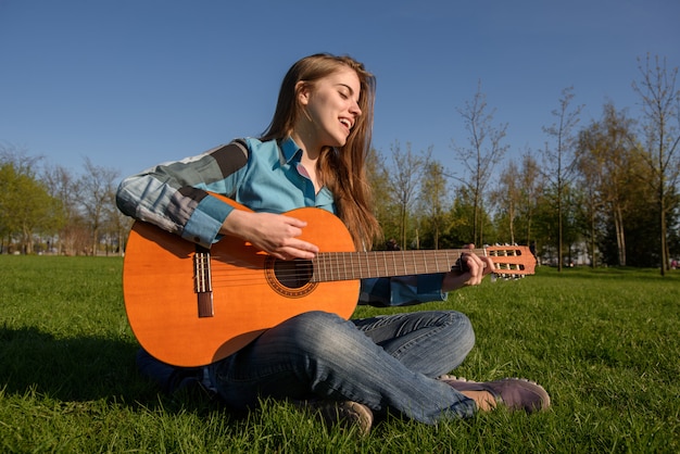 Giovane donna con la chitarra all'aperto su erba nel parco