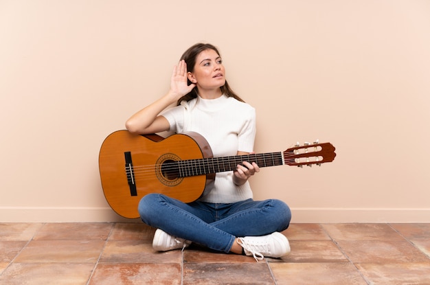 Young woman with guitar sitting on the floor listening something