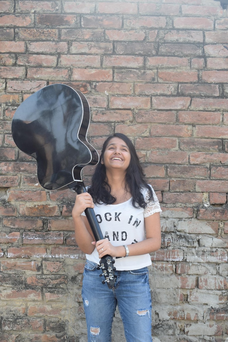 फोटो young woman with guitar standing against brick wall