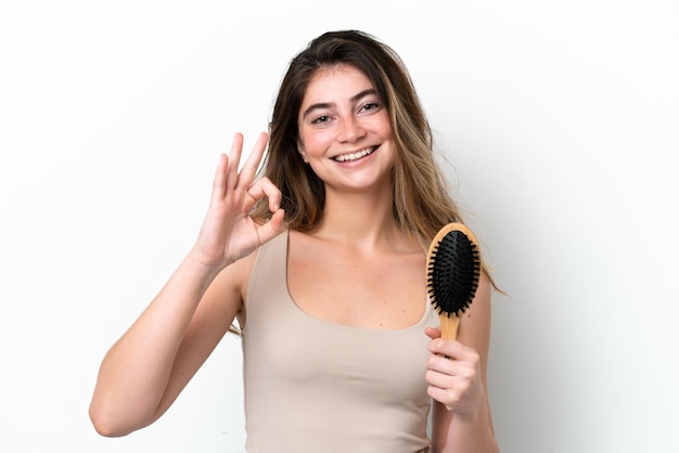 Young woman with hair comb isolated on white background showing ok sign with fingers