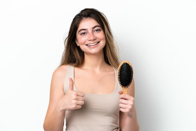 Young woman with hair comb isolated on white background with thumbs up because something good has happened