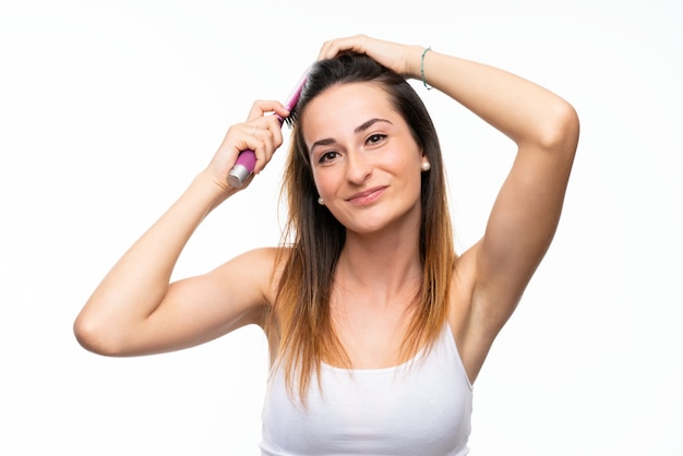 Giovane donna con il pettine dei capelli sopra la parete bianca isolata