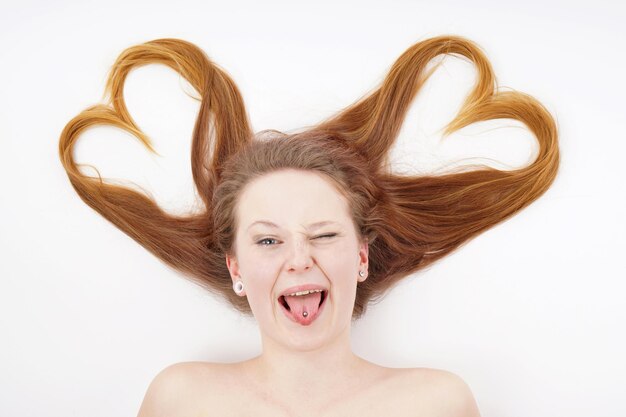Фото Молодая женщина с волосами в форме сердца и подмигивает, высунув язык.