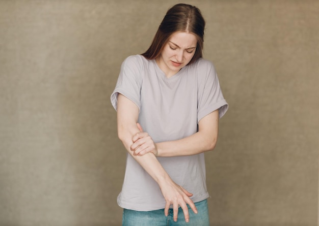 Молодая женщина с конвульсиями рук болит на коричневом фоне