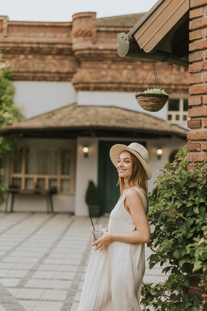 リゾート ガーデンで冷たいレモネードを飲む帽子を持つ若い女性