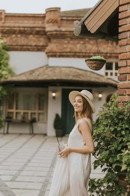 Young woman with hat drinking cold lemonade in the resort garden