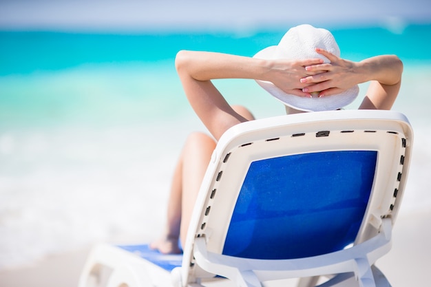 Giovane donna con cappello su un lettino in spiaggia tropicale