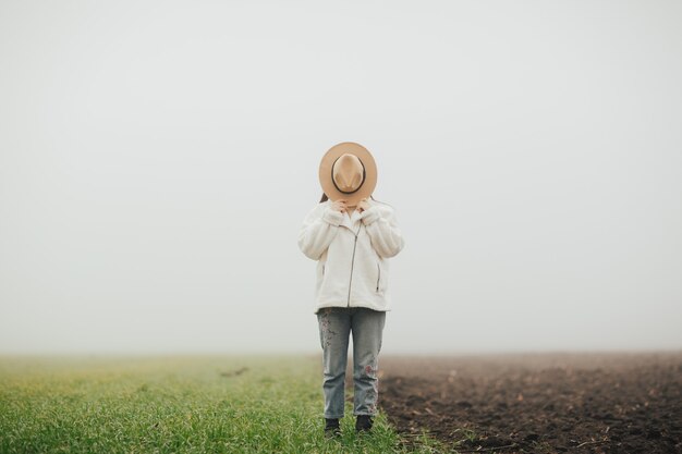 Young woman with hat standing on the green grass field and earth.